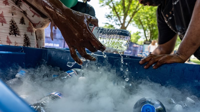 Un vendedor extrae una botella de agua de un depósito que usa hielo seco para mantenerla fría,...