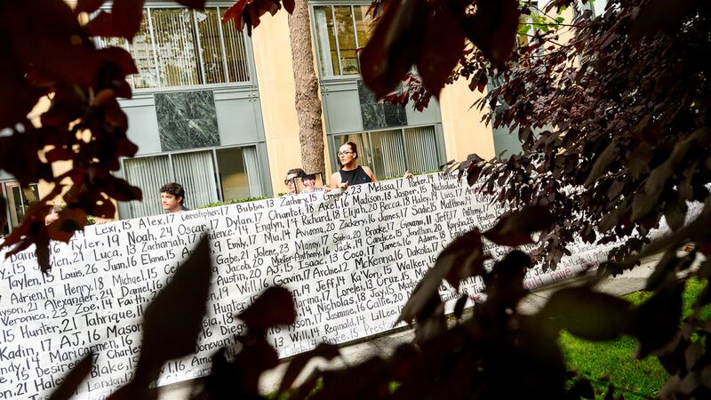 Lennon Torres de Heat Initiative sostiene un cartel con los nombres de jóvenes que, según...